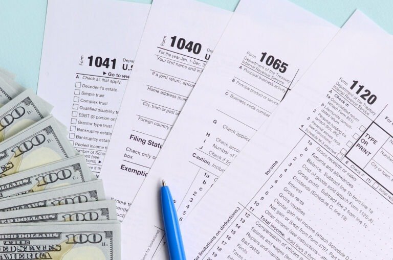 Tax forms lies near hundred dollar bills and blue pen on a light blue background. Income tax return