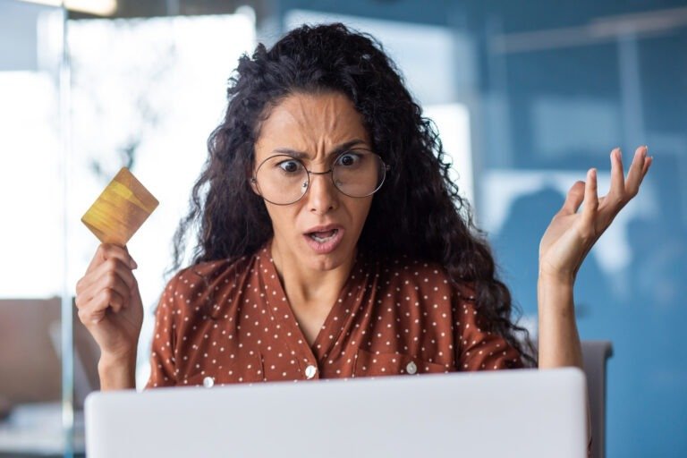 Upset and shocked business woman with bank credit card and laptop, female worker received rejection error at workplace inside office